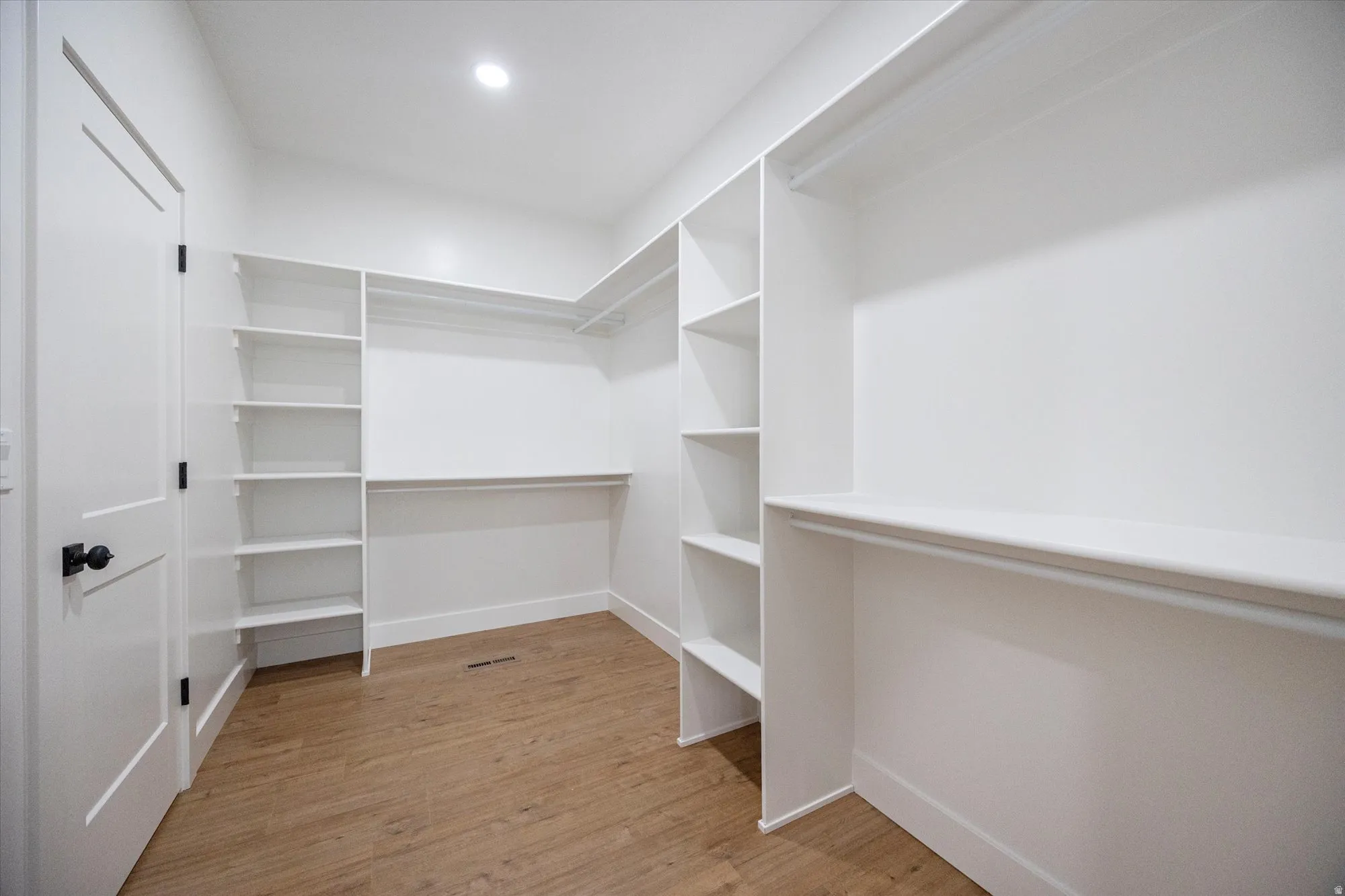 White closet with extensive built-in shelving, hanging rods, and wood-finish flooring