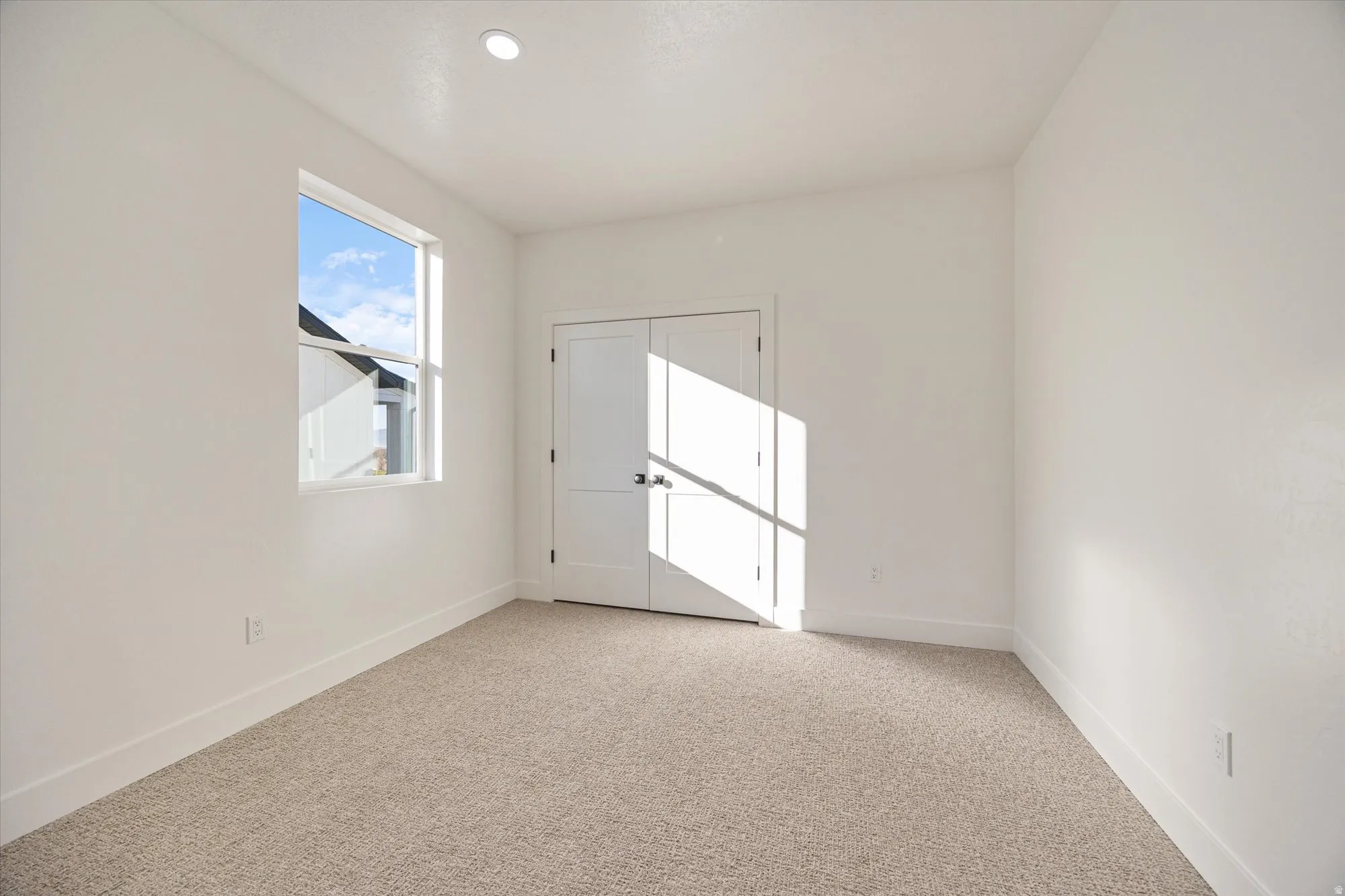 Bright room featuring light beige carpeting, white walls, and a single window