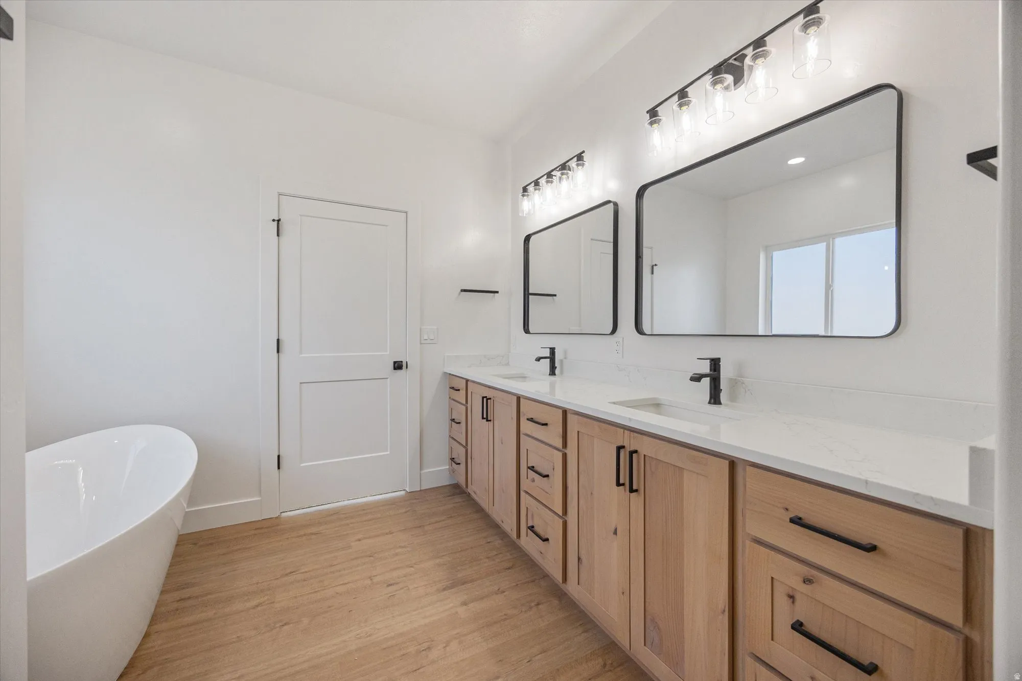 Double vanity with wood-finish cabinetry, white countertops, and matte black fixtures