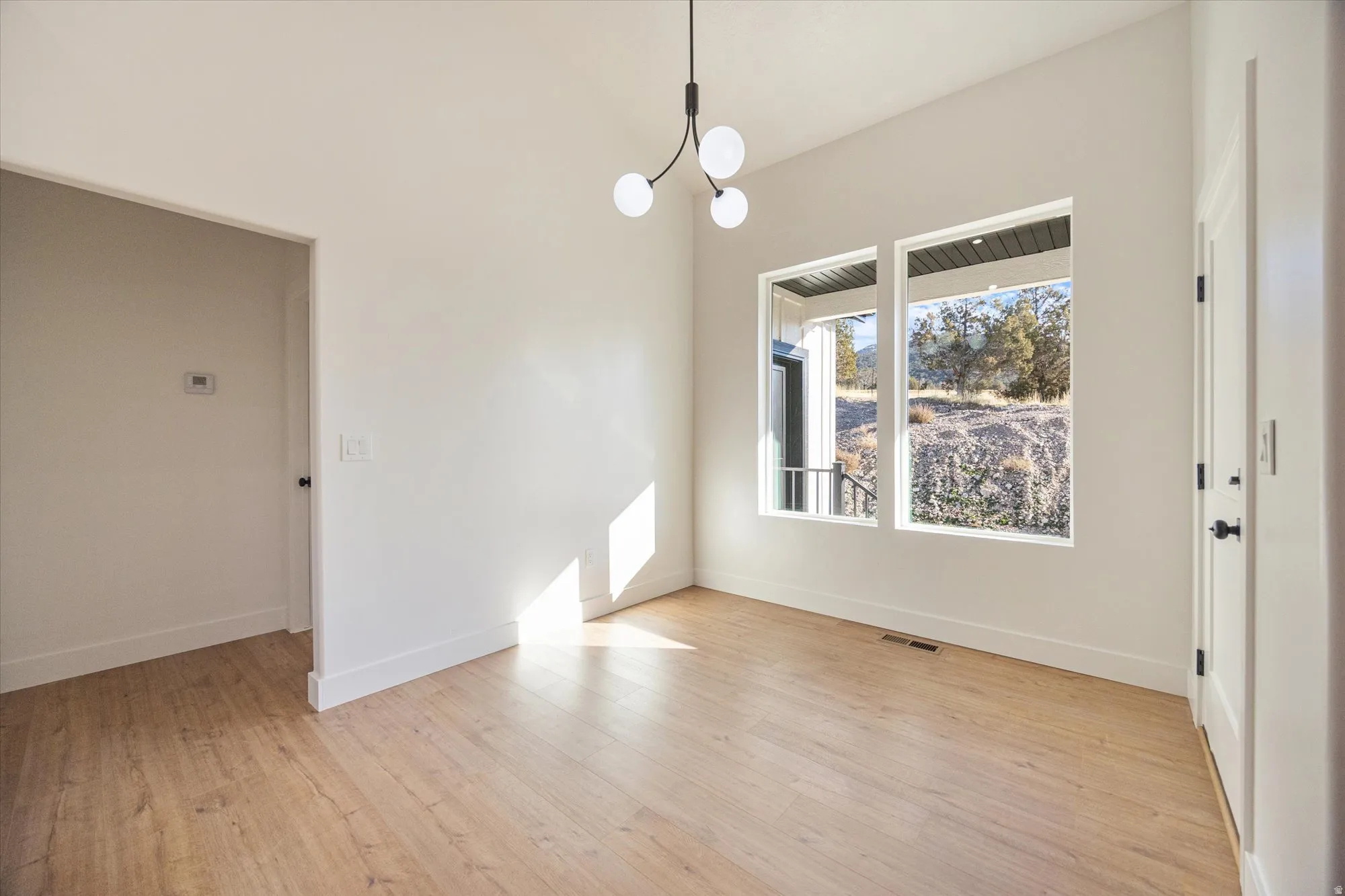 Bright interior space featuring a contemporary chandelier, two large windows, wood-finish flooring, and white baseboards