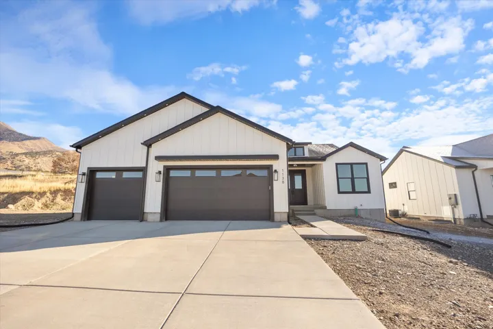 Modern farmhouse exterior featuring white vertical siding with dark trim, a two-car garage with frosted window panels, a dark entry door, and concrete driveway