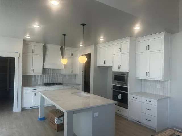 Modern kitchen featuring white shaker cabinetry, light wood-finish flooring, quartz countertops, and stainless steel appliances