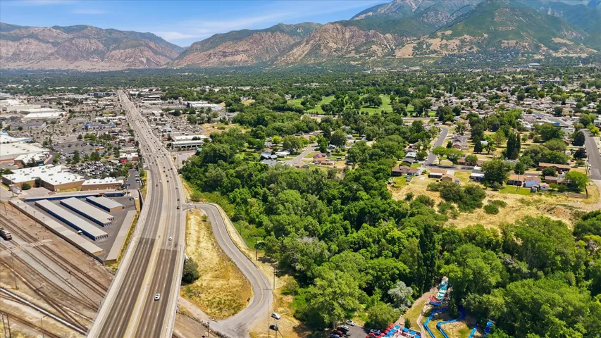 Expansive aerial perspective showcasing a mountainous backdrop, abundant mature trees, a multi-lane highway, and a residential area with varied rooflines