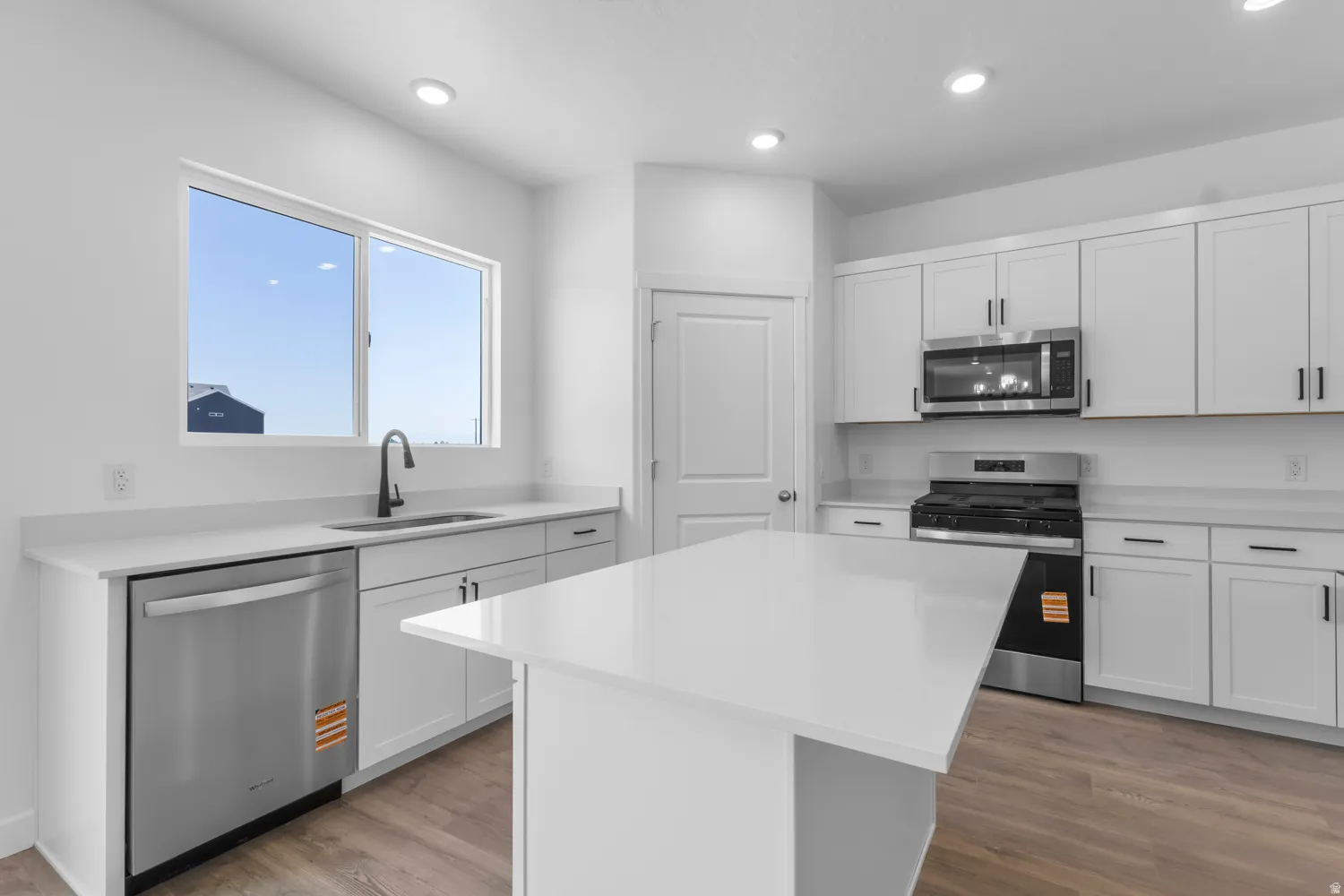 Kitchen featuring a central island, white shaker cabinetry, stainless steel appliances, and light-toned wood-finish flooring