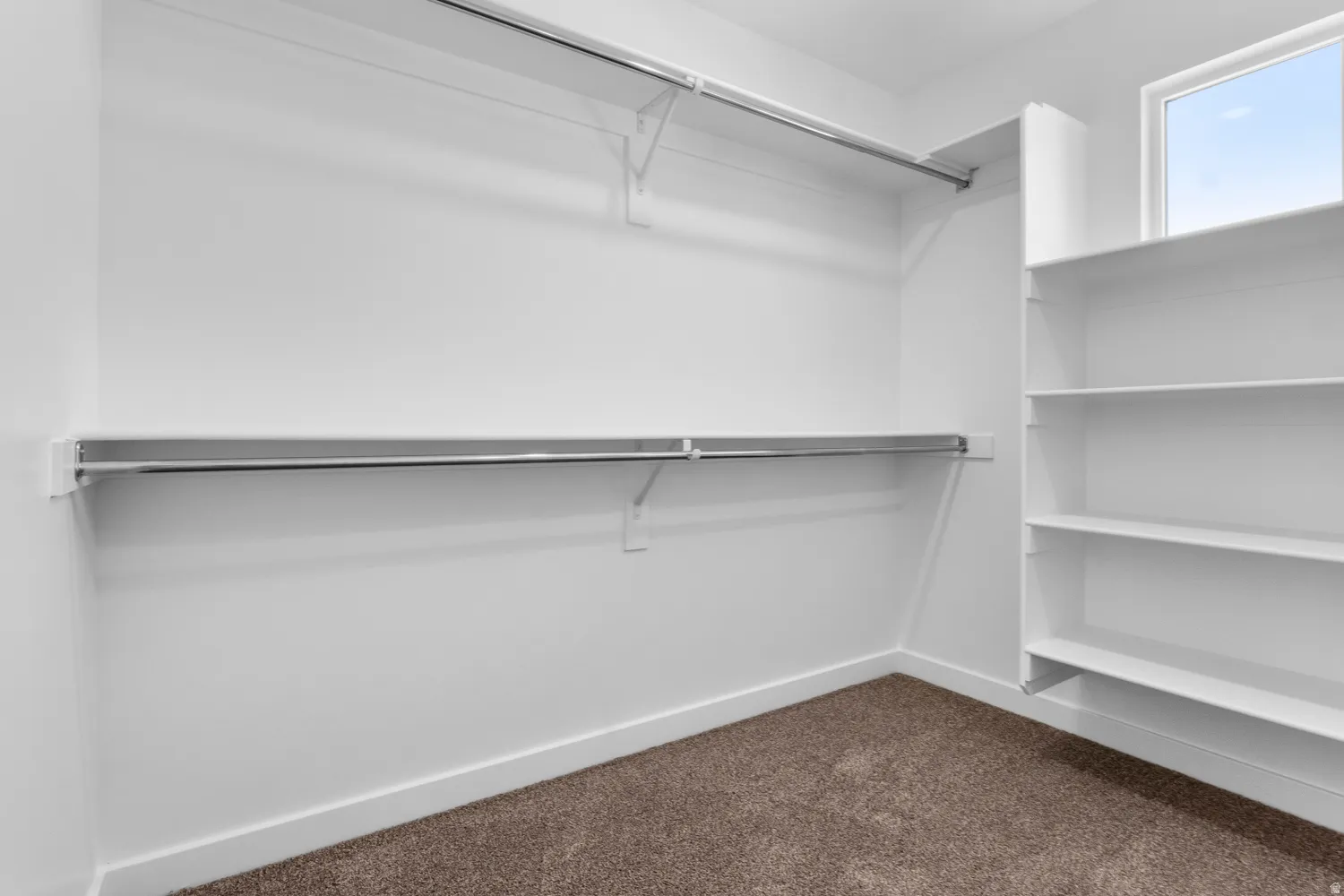 Walk-in closet with ample storage solutions featuring built-in shelving, chrome hanging rods, and a high window