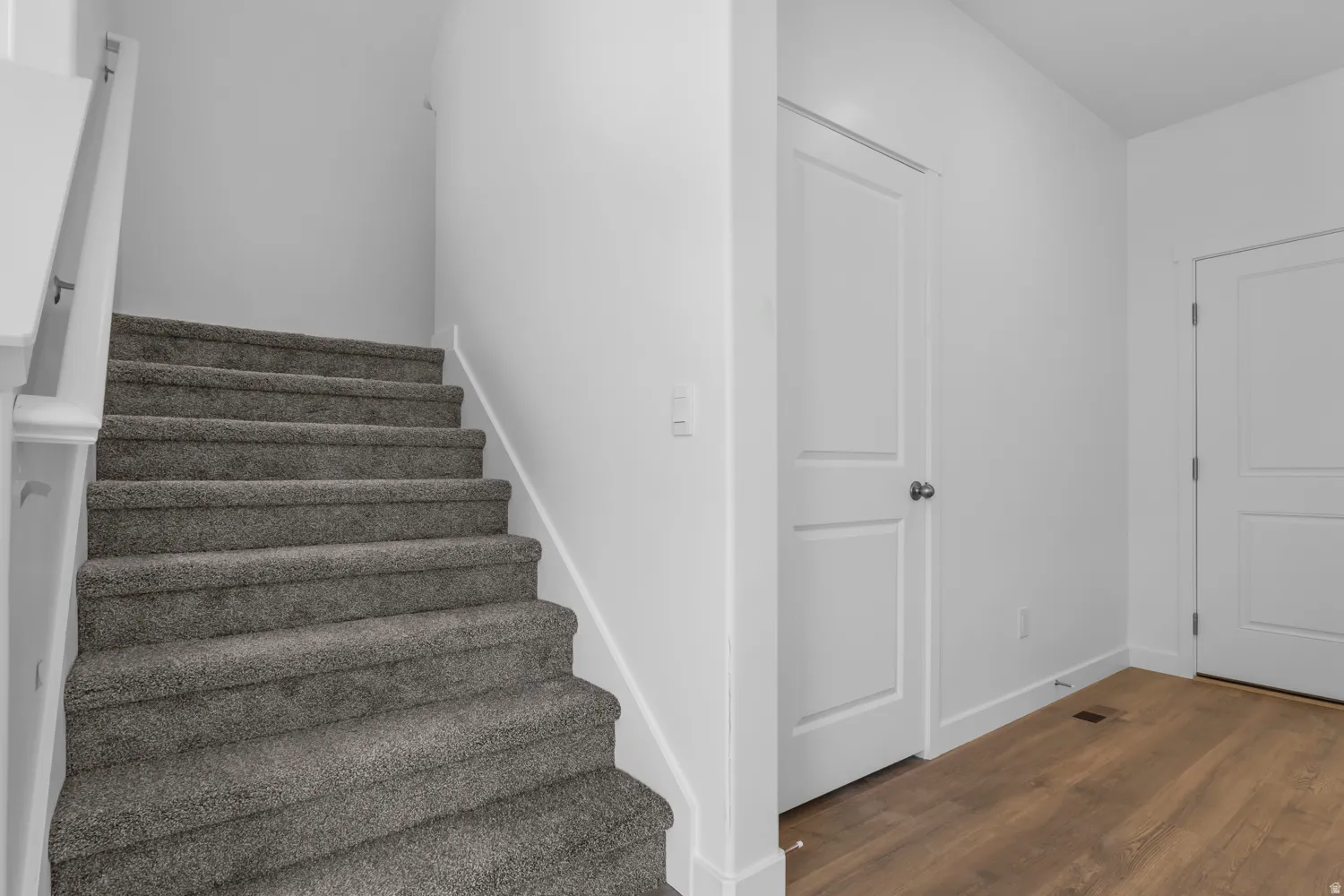 Carpeted staircase with white balustrade and handrail, complementing white interior doors, white baseboards, and wood-finish flooring