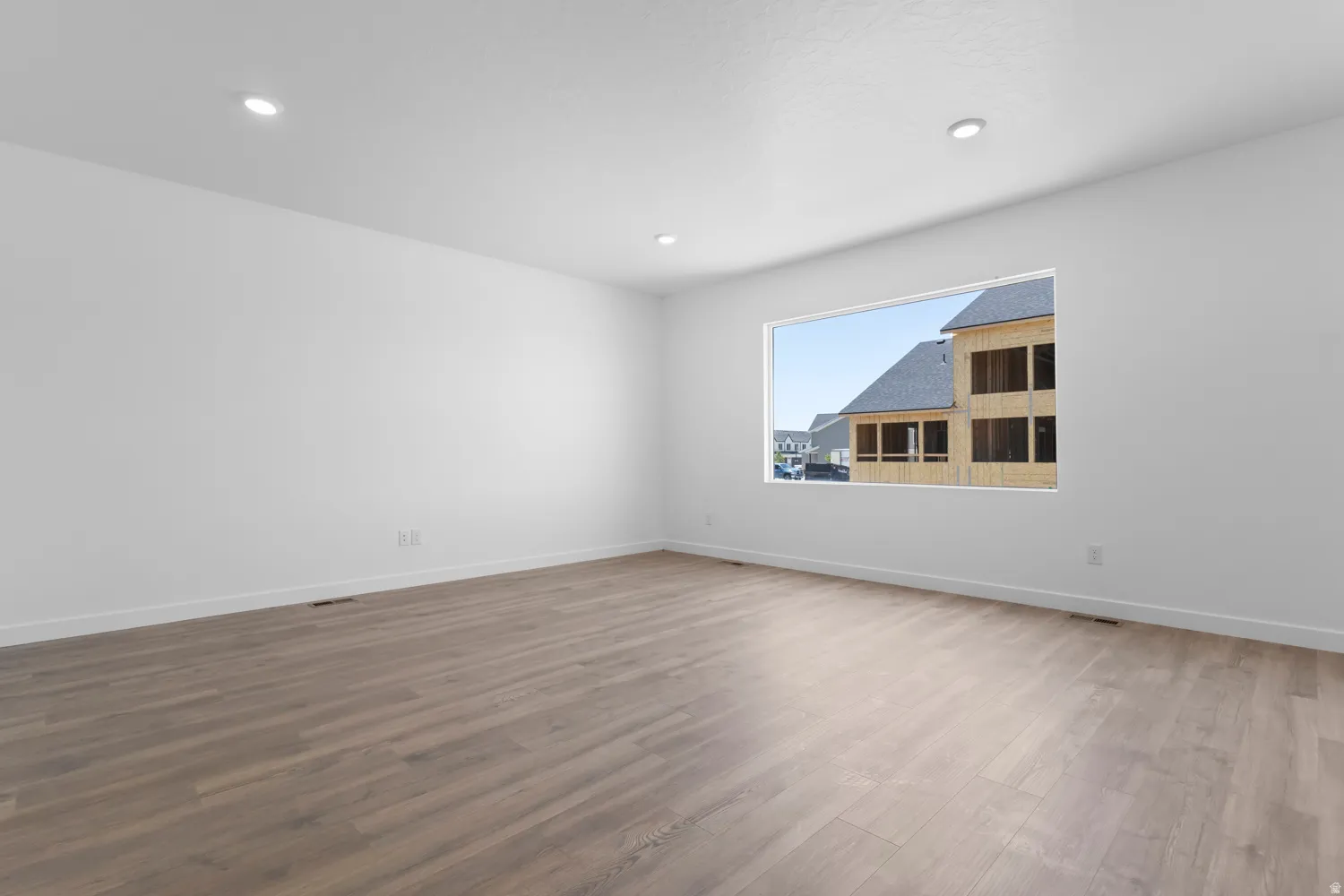 Spacious room featuring light wood-finish flooring, recessed lighting, and a large window