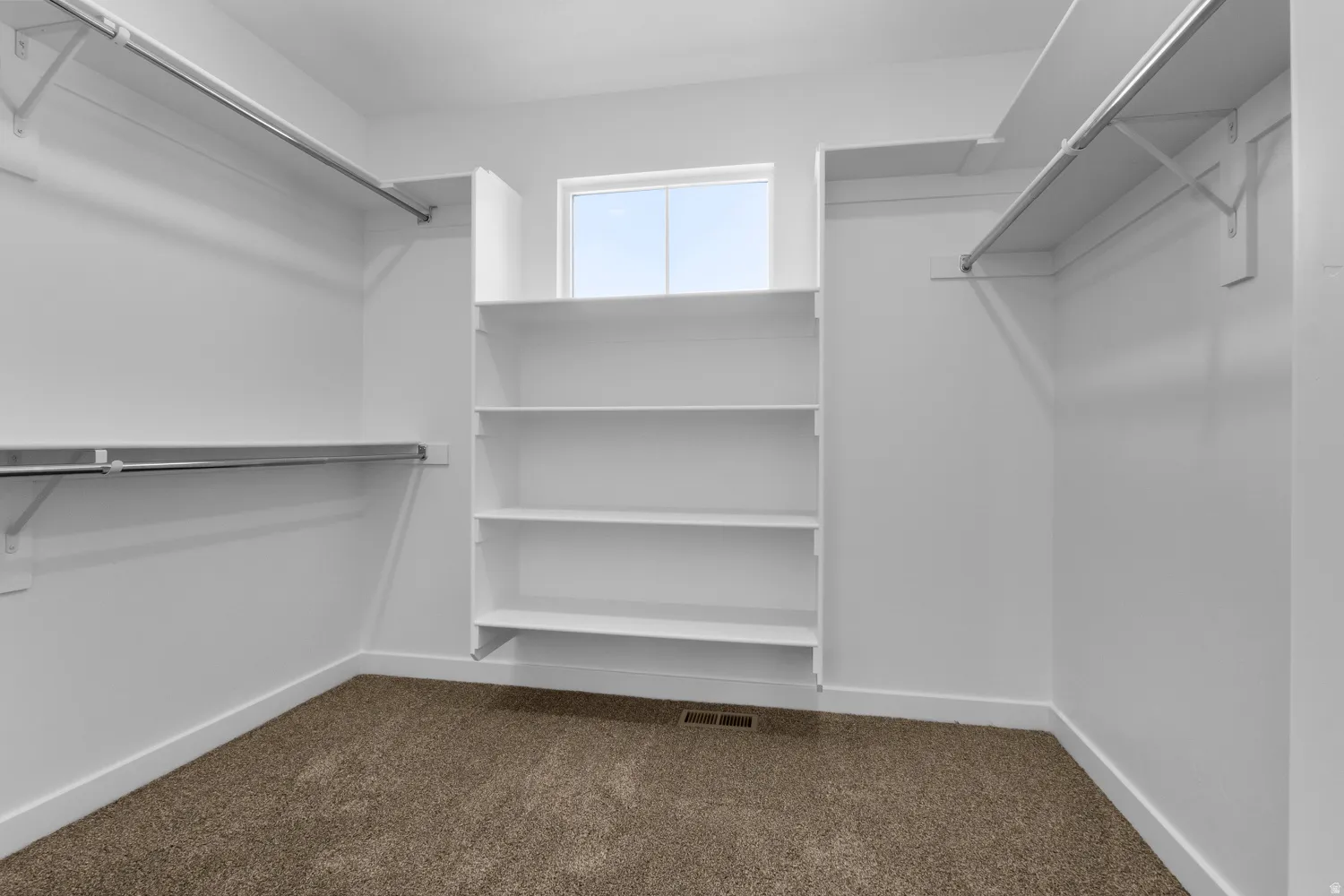 Walk-in closet with integrated shelving, multiple clothing rods, and a window for natural light