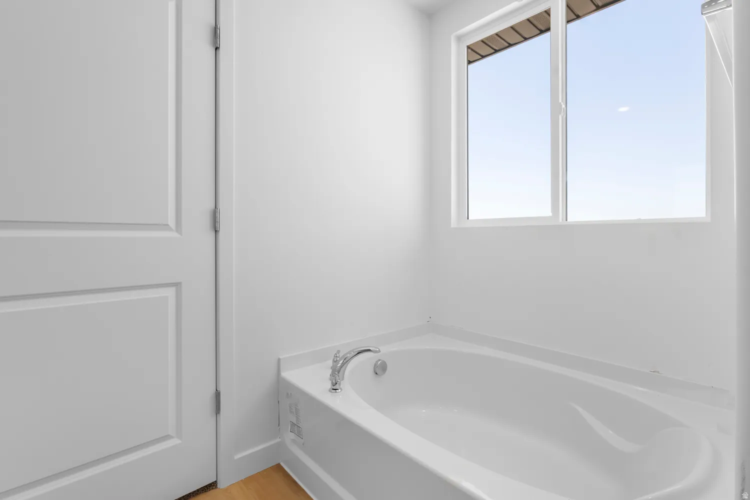 White soaking tub featuring a chrome faucet, a white paneled door, and a white-framed window
