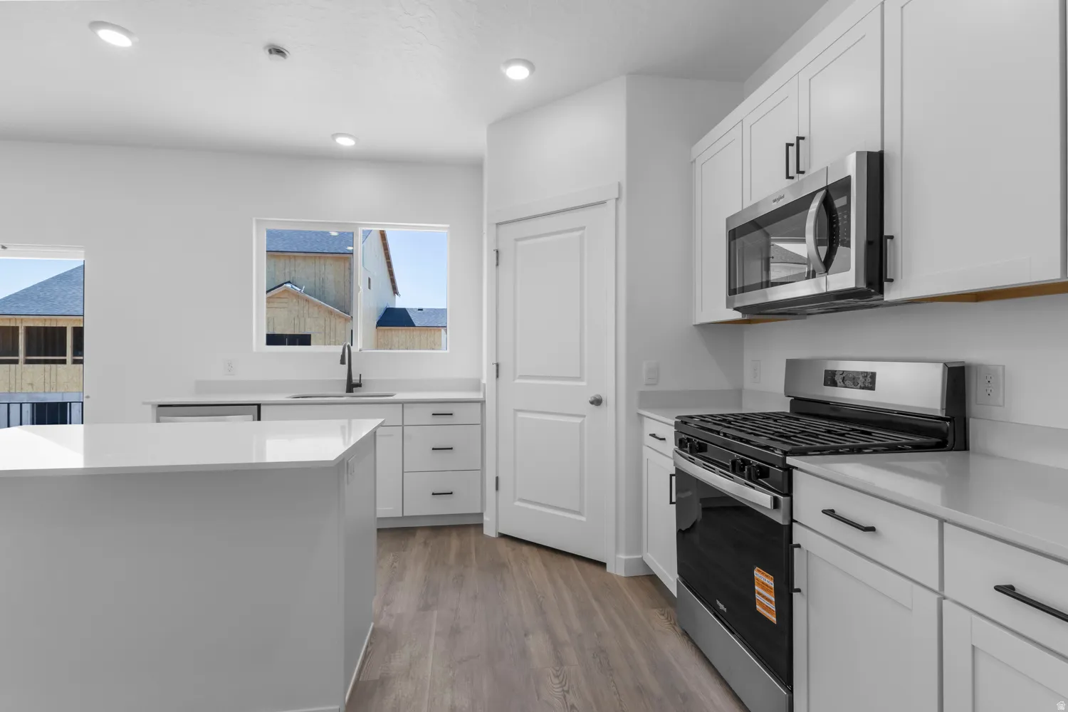 Bright kitchen featuring white cabinetry, light-toned countertops, and wood-finish flooring