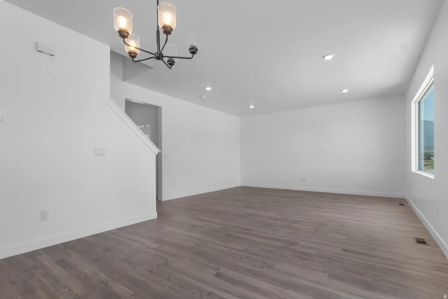 Spacious room featuring wood-finish flooring, white baseboards, and a modern chandelier with seeded glass shades