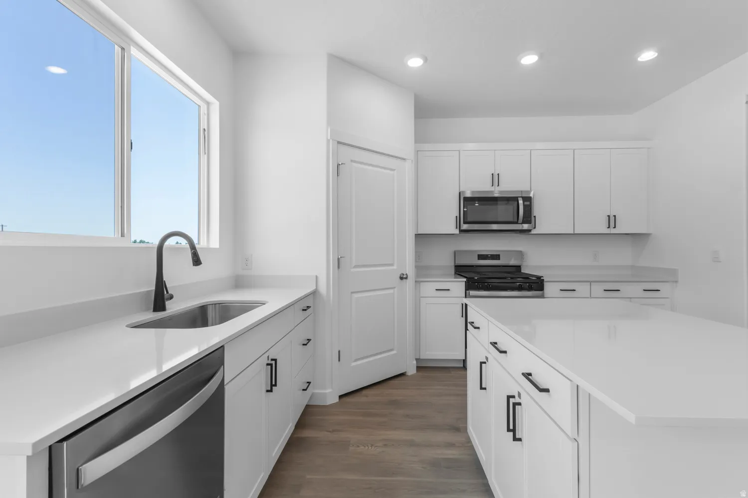 Kitchen featuring white cabinetry, light countertops, wood-finish flooring, recessed lighting, and a stainless steel appliance package including a gas range, microwave, and dishwasher