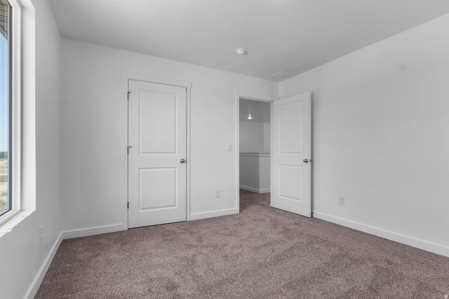 Carpeted room featuring a large window, a two-panel door, and white baseboards