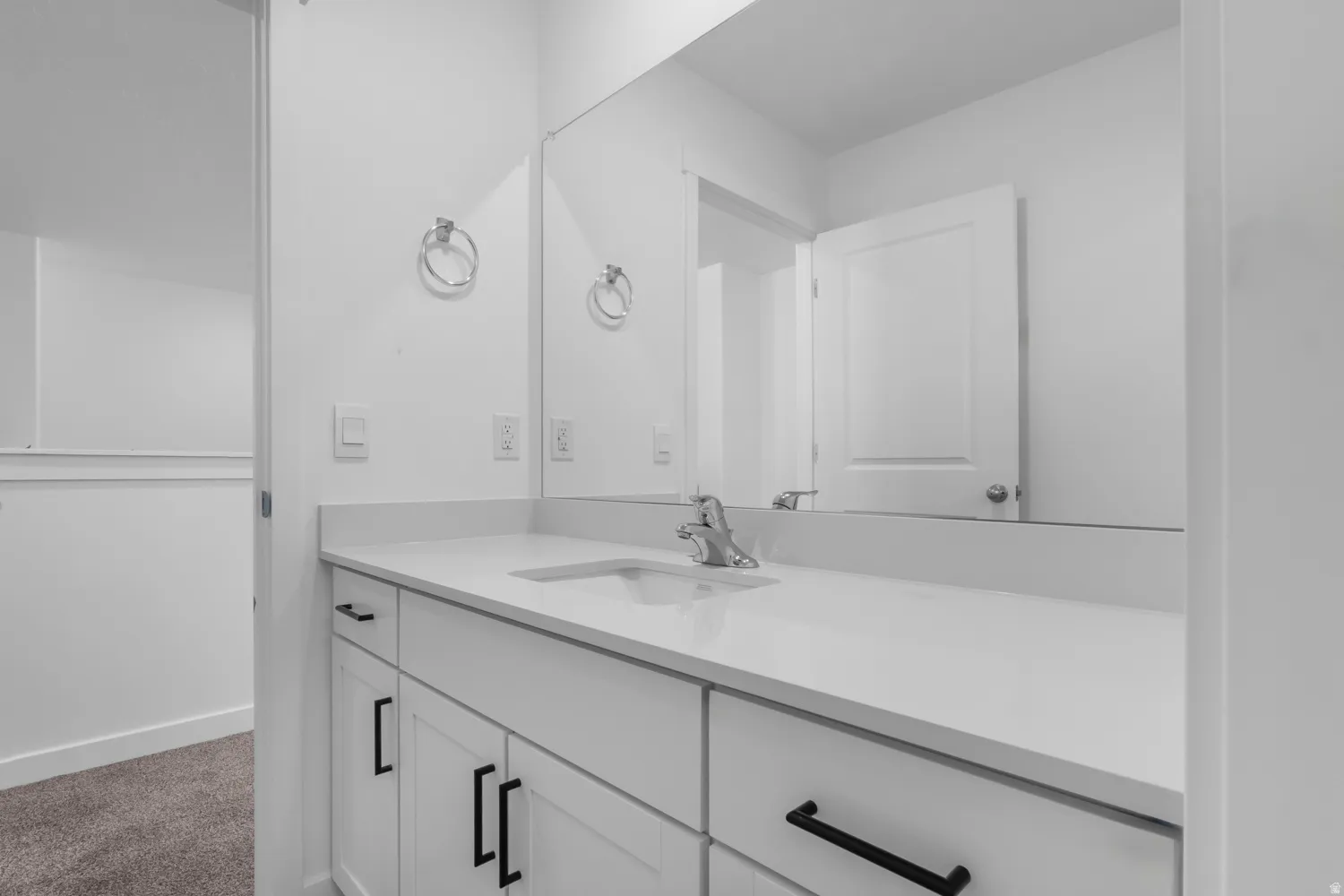 Bathroom vanity featuring a quartz countertop, integrated rectangular sink, chrome faucet, and matte black cabinet hardware