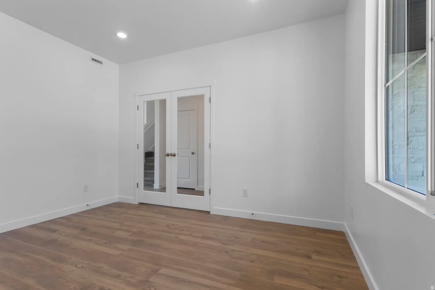 Spacious room with wood-finish flooring, recessed lighting, and a large window