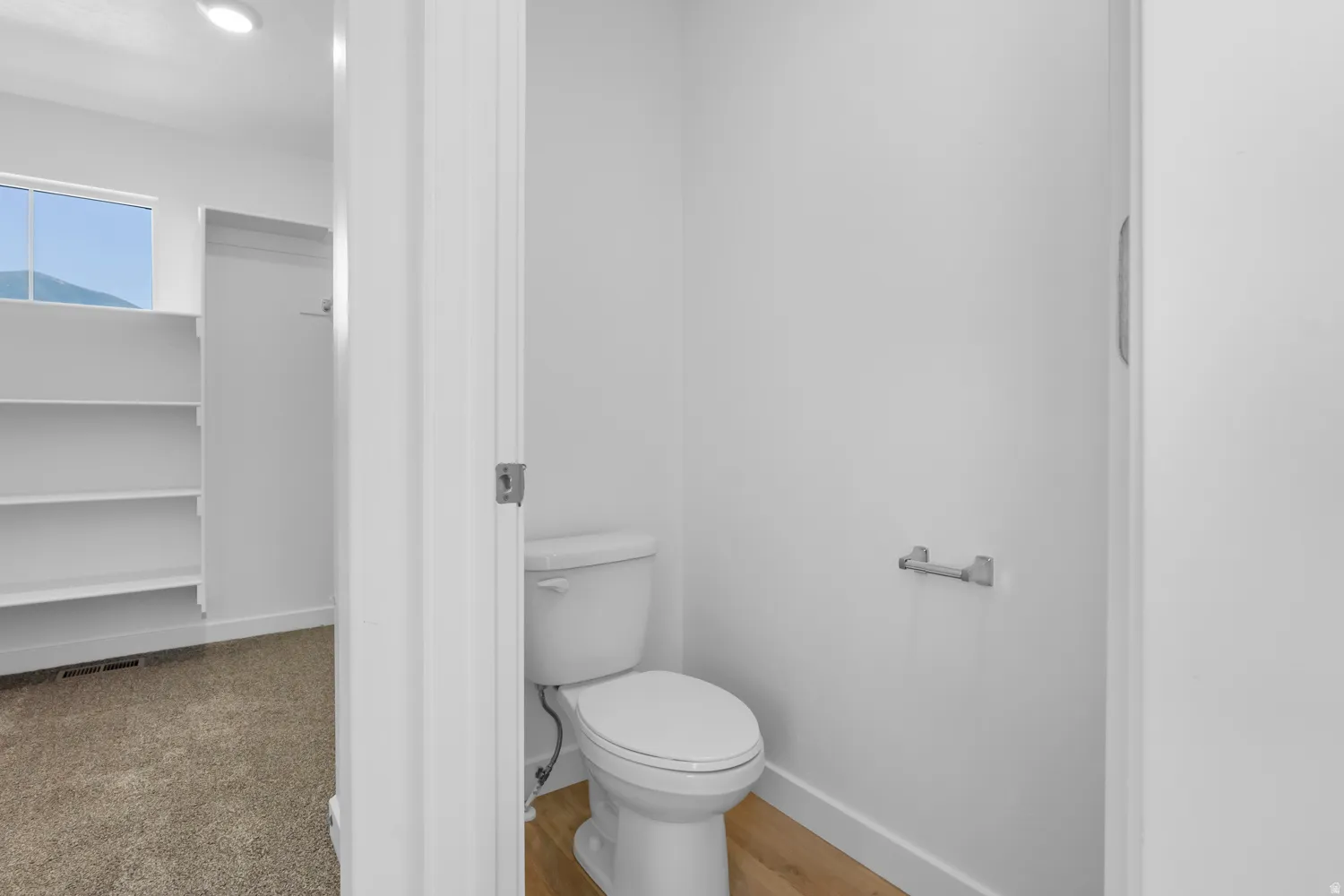 Powder room featuring a standard toilet, wood-finish flooring, and a stainless steel toilet paper holder