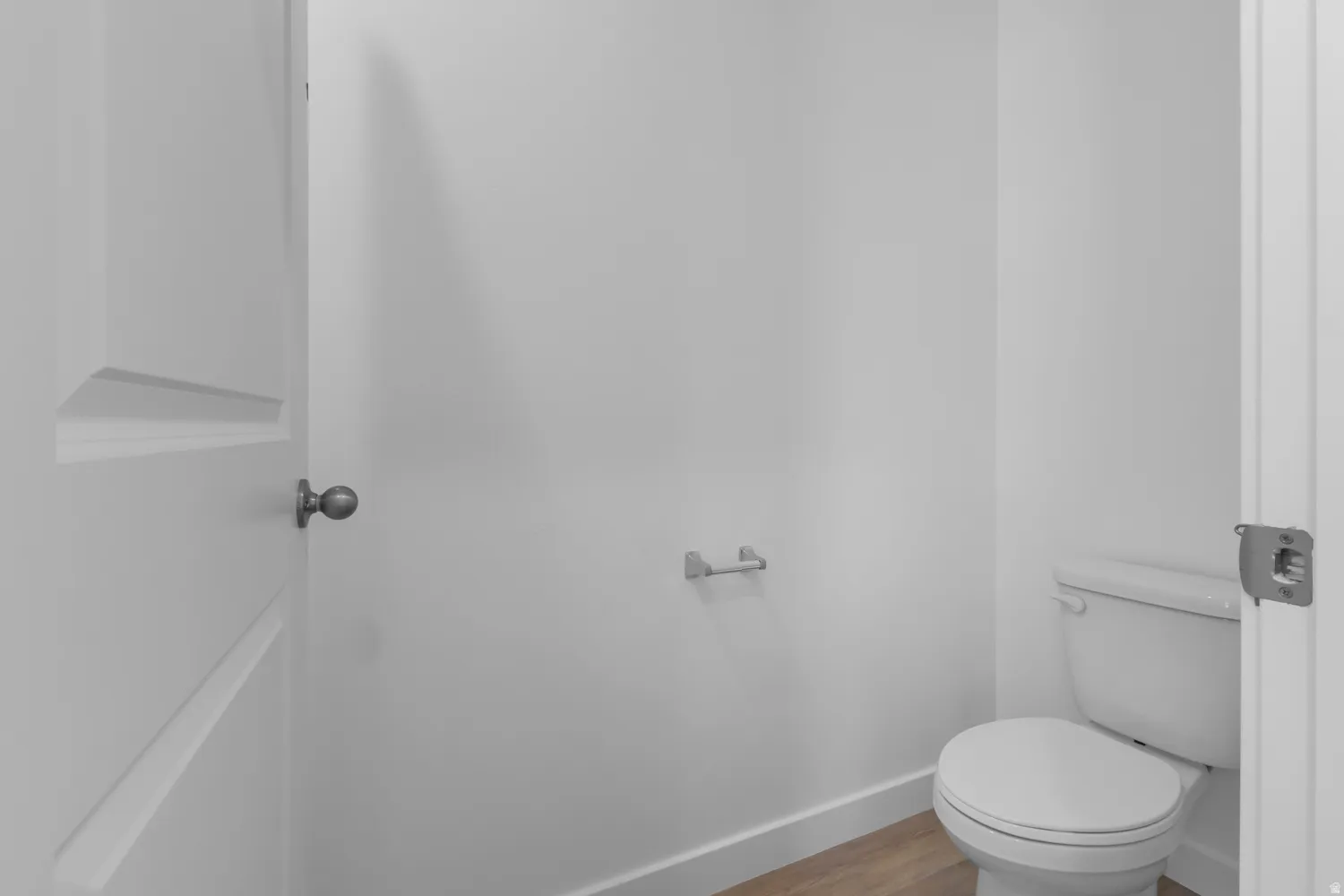 Powder room featuring a white toilet, light wood-finish flooring, and crisp white walls
