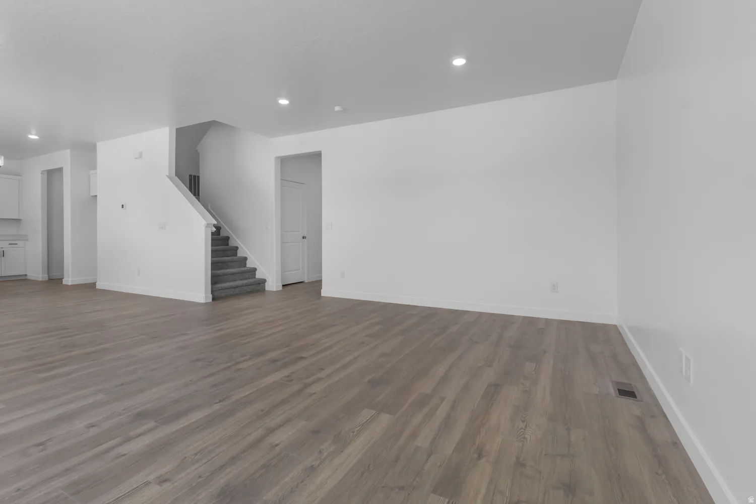 Spacious open-concept living area featuring wood-finish flooring, recessed lighting, and crisp white walls