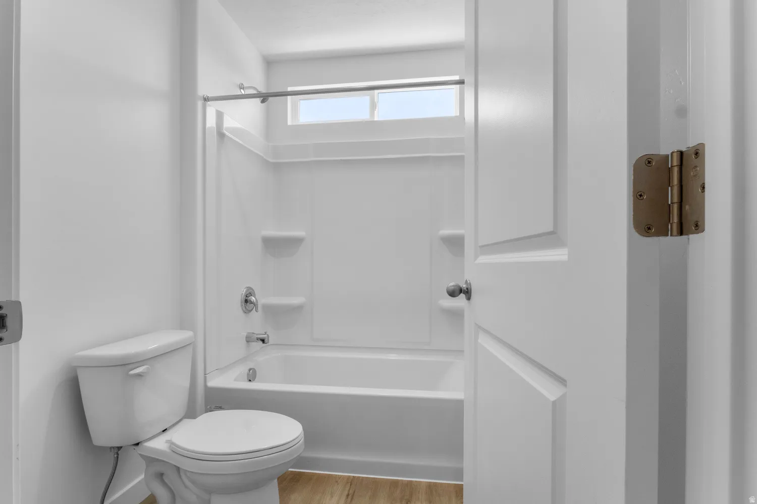 Bathroom featuring a white tub and shower combination with an integrated storage shelf, a white toilet, and wood-finish flooring
