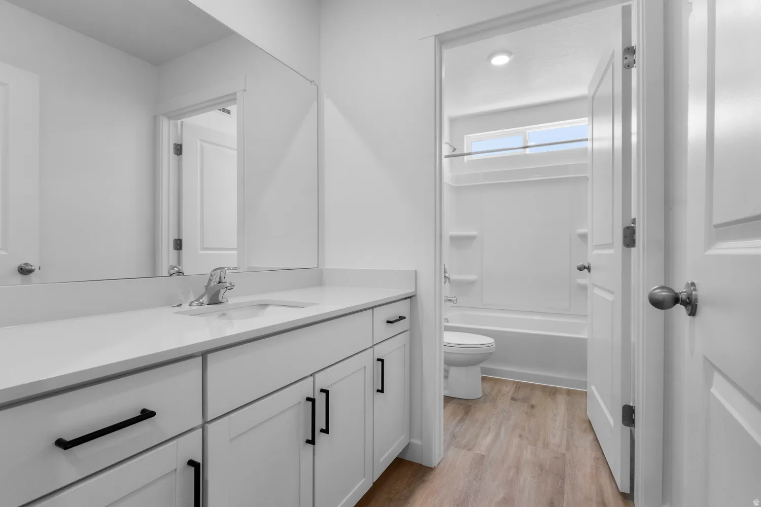 Modern bathroom featuring a single vanity with a white countertop, undermount sink, and shaker-style cabinetry with black hardware