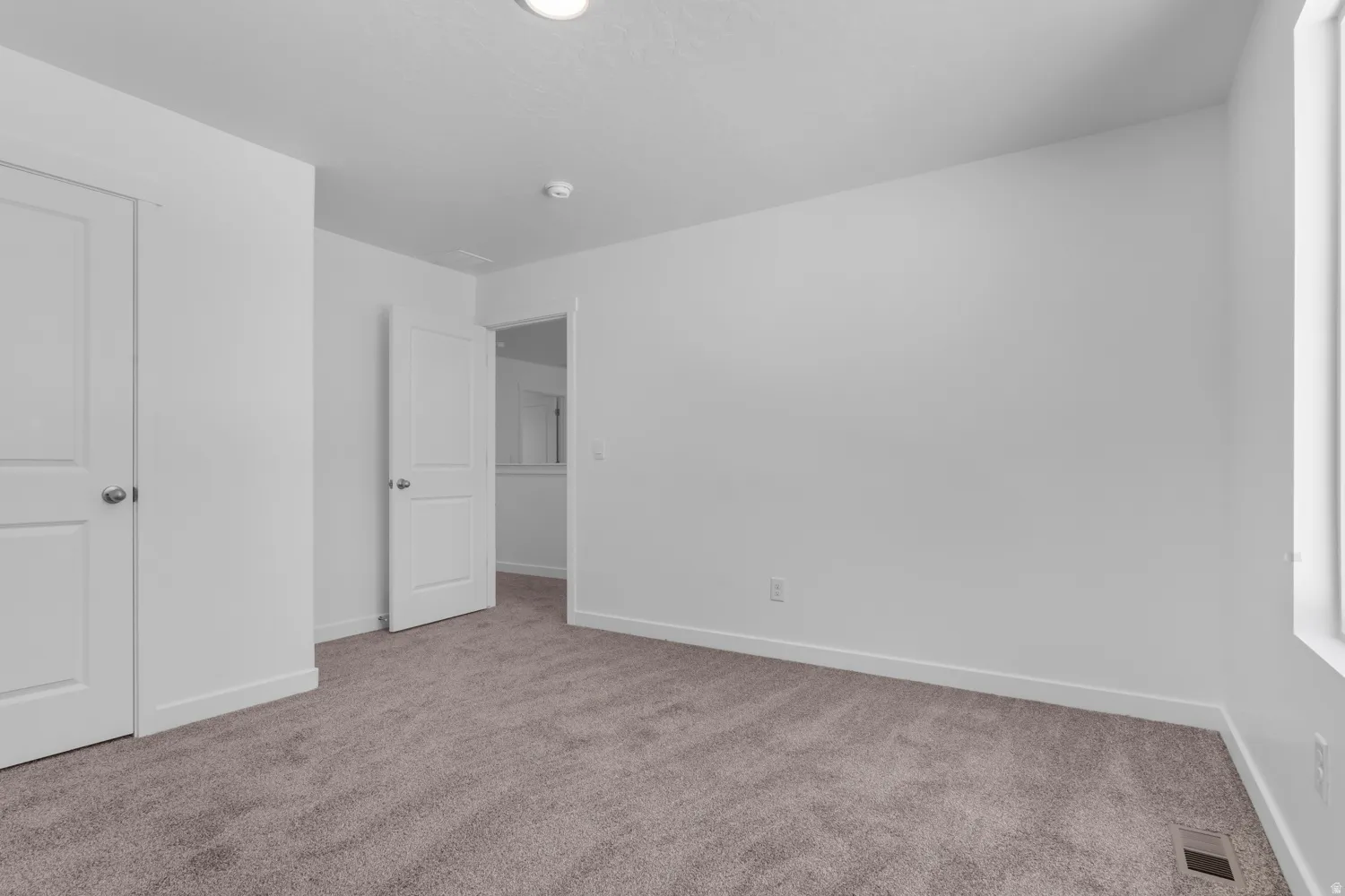 Carpeted room featuring white walls, a single window, and multiple white doors with brushed nickel hardware