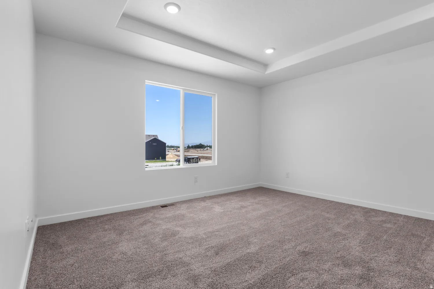 Spacious room featuring a tray ceiling with recessed lighting, a large window providing natural illumination, plush carpeting, and crisp white walls