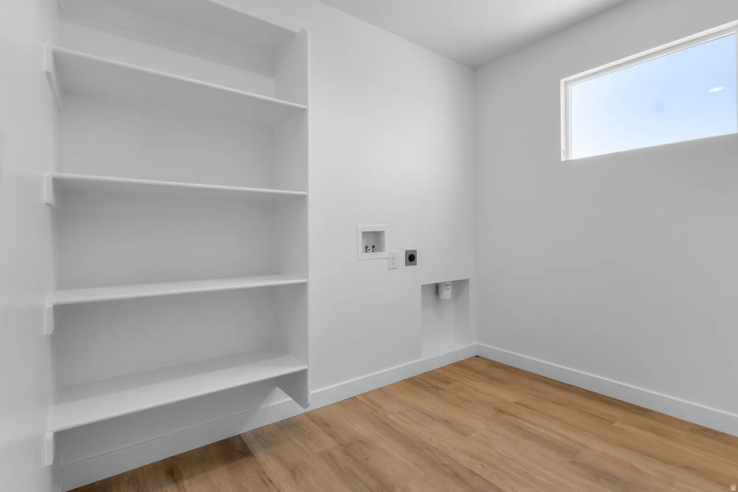 Dedicated utility area featuring wood-finish flooring, built-in shelving, a high transom window, and appliance hookups