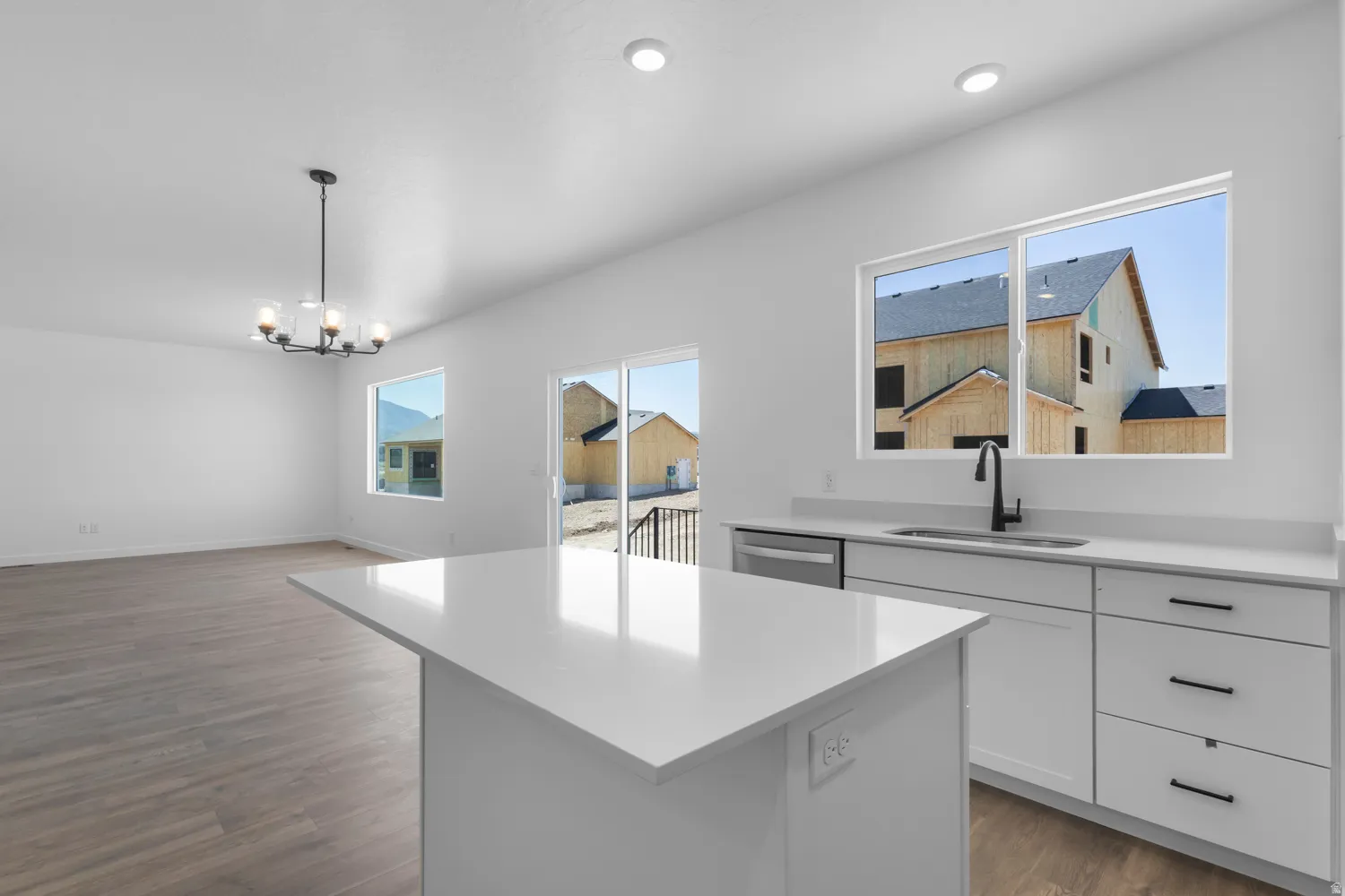 Bright open-concept kitchen and living area featuring a central island with a solid surface countertop, white cabinetry with black hardware, a stainless steel dishwasher, and wood-finish flooring