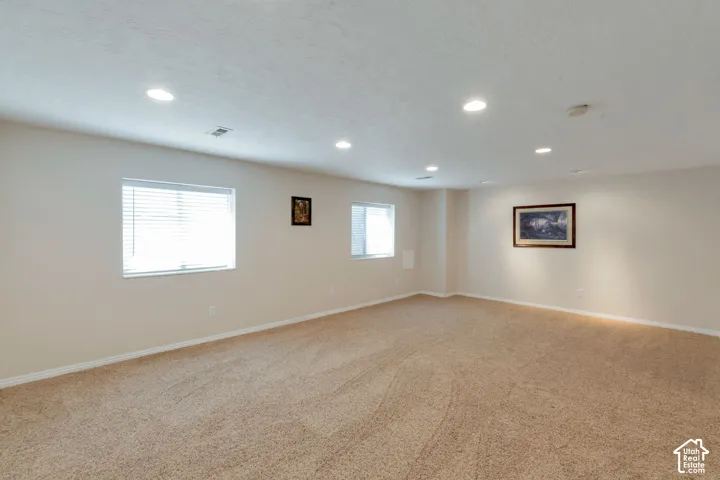Spacious room featuring neutral carpeting, light-toned walls, recessed lighting, and multiple windows with blinds