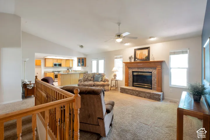 Spacious living room featuring vaulted ceilings, a stone-surround fireplace with a wood mantle, and bright windows