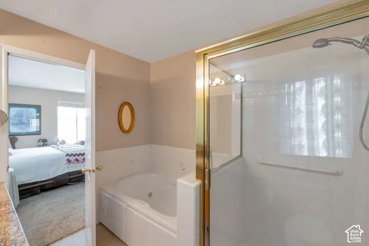 Bathroom featuring a corner jetted soaking tub, a glass-enclosed shower with gold-finish trim, white subway tile shower surround, and a chrome shower head