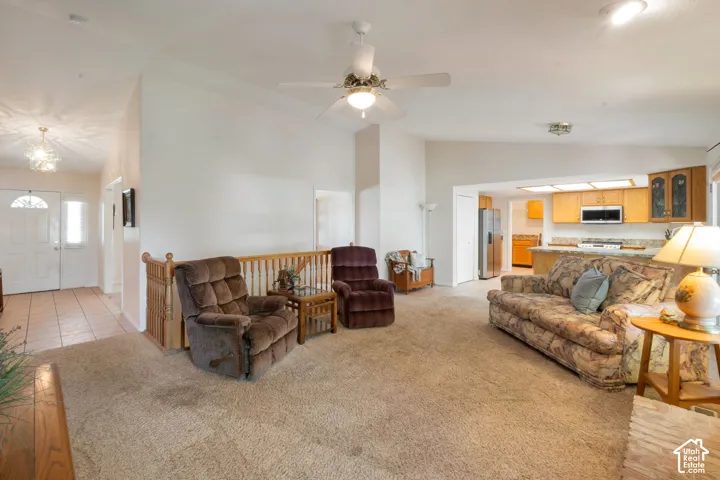 Spacious living area featuring vaulted ceilings, ceiling fan, and carpet flooring
