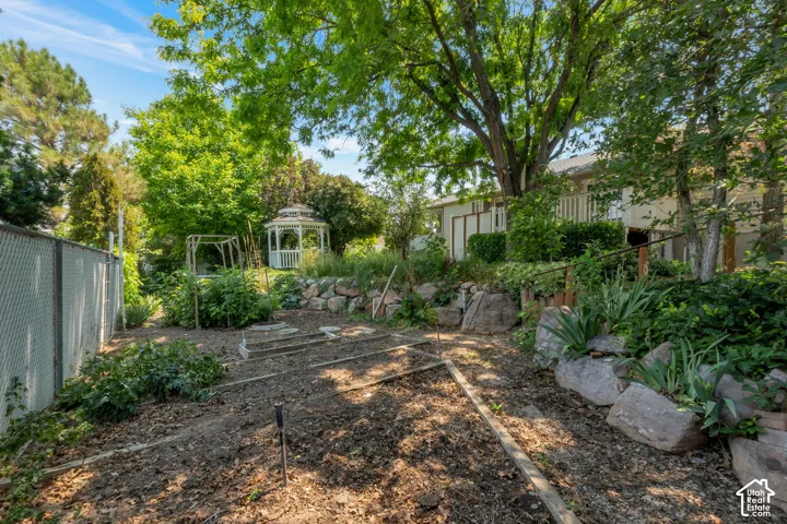 Expansive backyard featuring a white gazebo, terraced landscaping with rock retaining elements, established garden beds, mature trees, and a chain-link fence