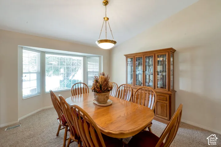 Dining area featuring a prominent bay window with blinds, vaulted ceiling, and carpeted flooring