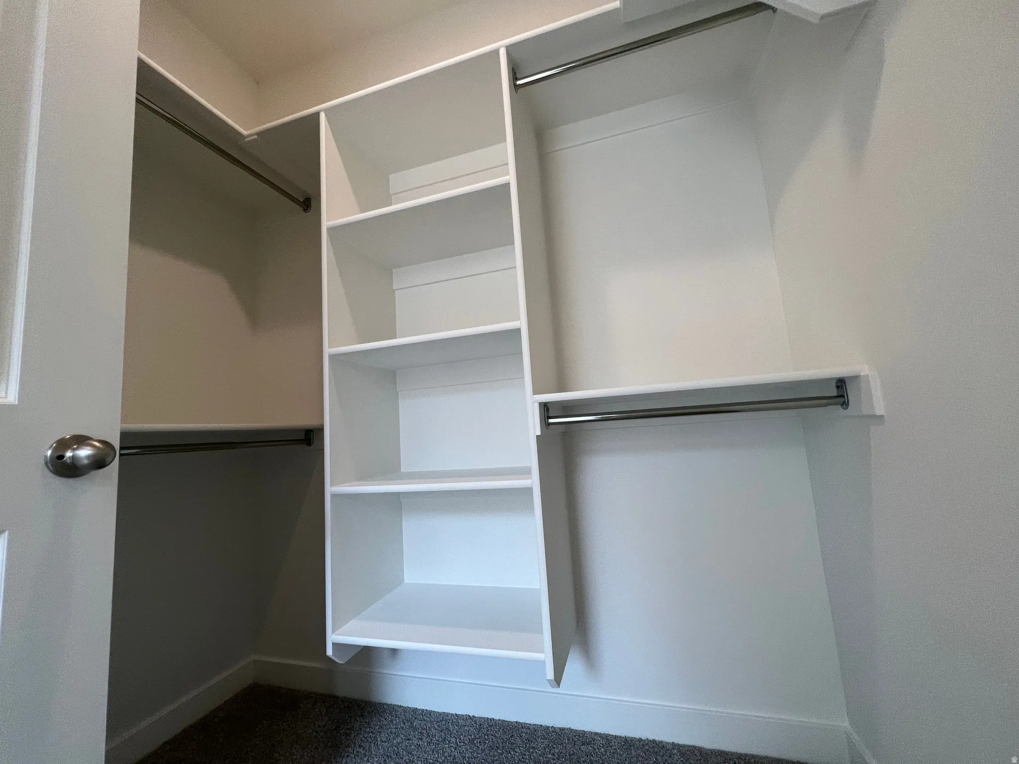 Walk-in closet featuring white built-in shelving, multiple hanging rods, and dark gray carpet flooring