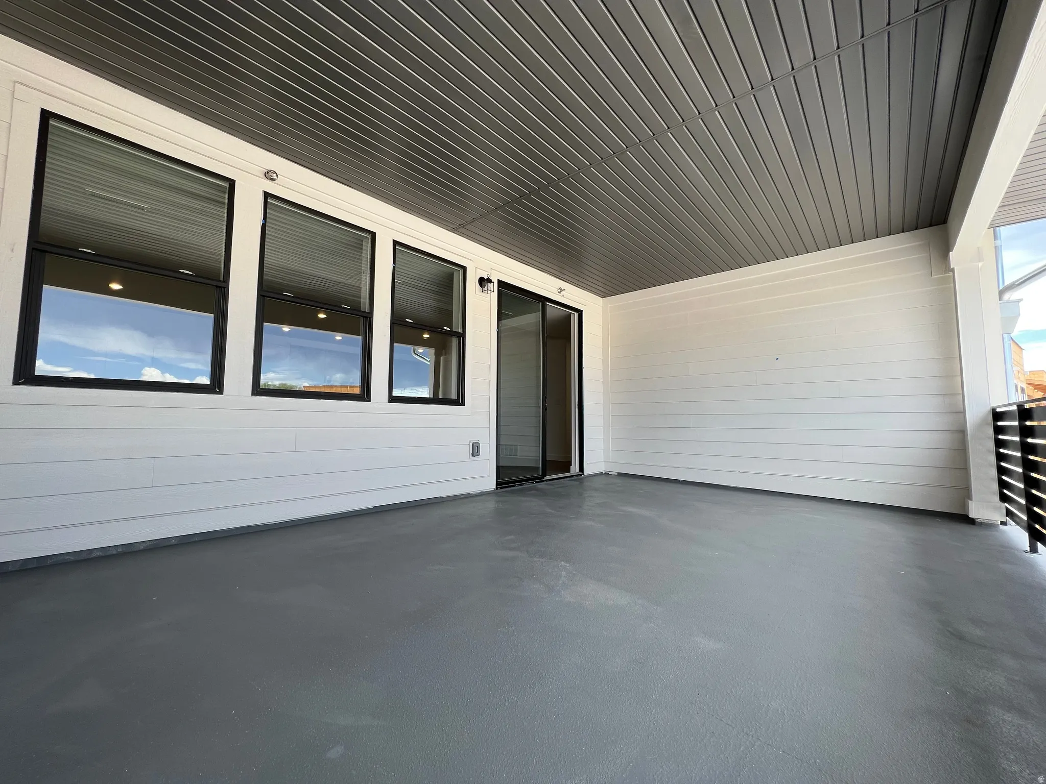 Expansive covered outdoor patio featuring a gray finished concrete floor, white horizontal siding, and a slatted ceiling with recessed lighting