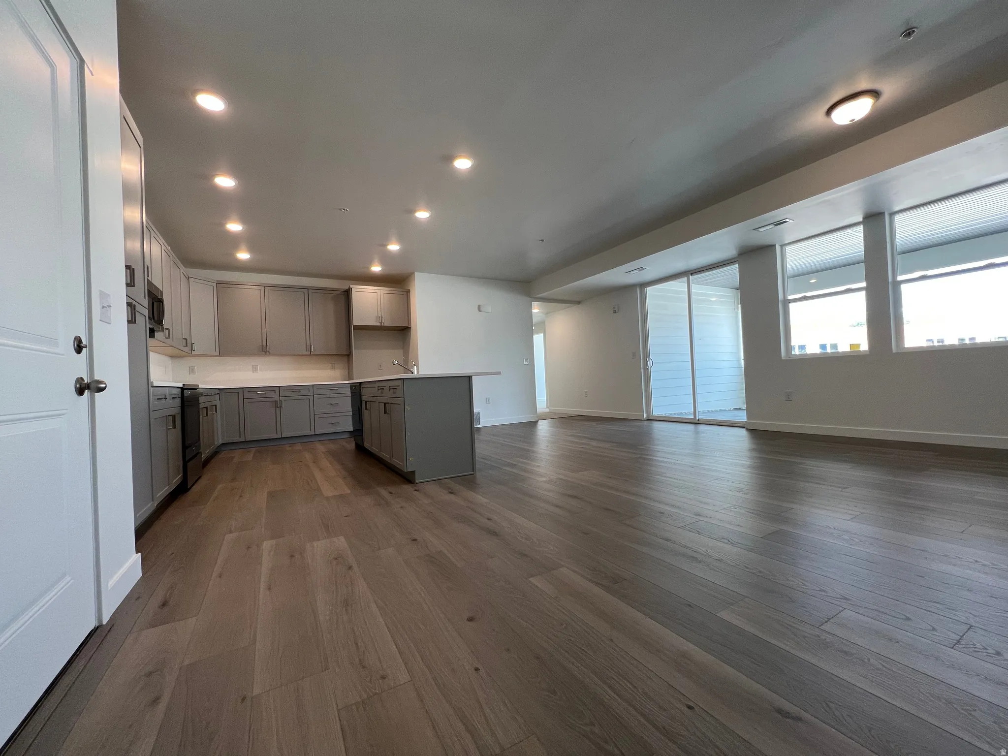 Open-concept living area featuring wood-finish flooring, a contemporary kitchen with gray cabinetry, white countertops, and a kitchen island