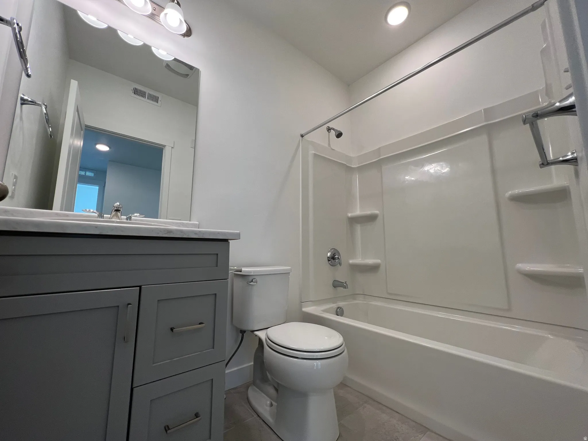 Bathroom featuring a white bathtub with a built-in shower system, a gray vanity with a light-colored countertop, and a modern toilet