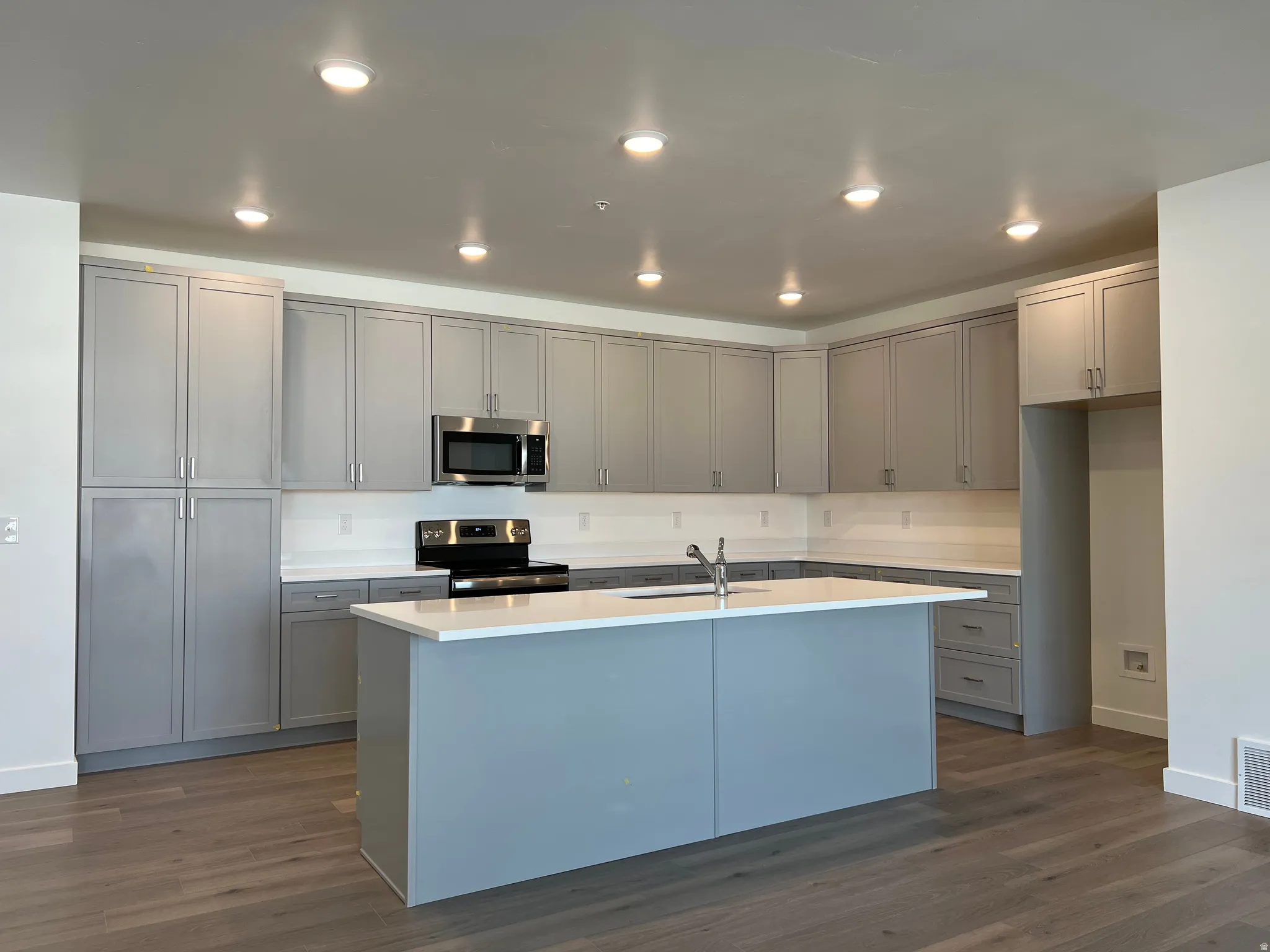 Modern kitchen featuring gray cabinetry, stainless steel appliances, a center island with sink, white countertops, and wood-finish flooring