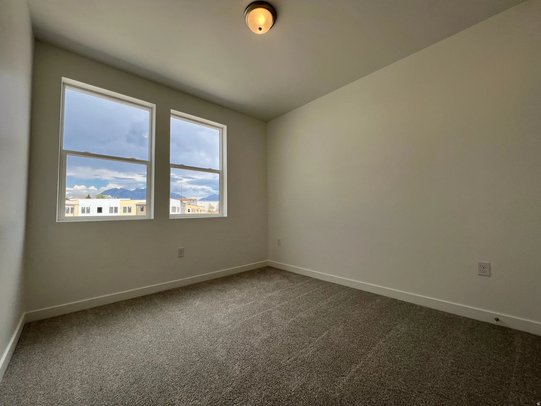 Bright interior space featuring two windows with surrounding white trim, neutral wall paint, and gray carpet flooring
