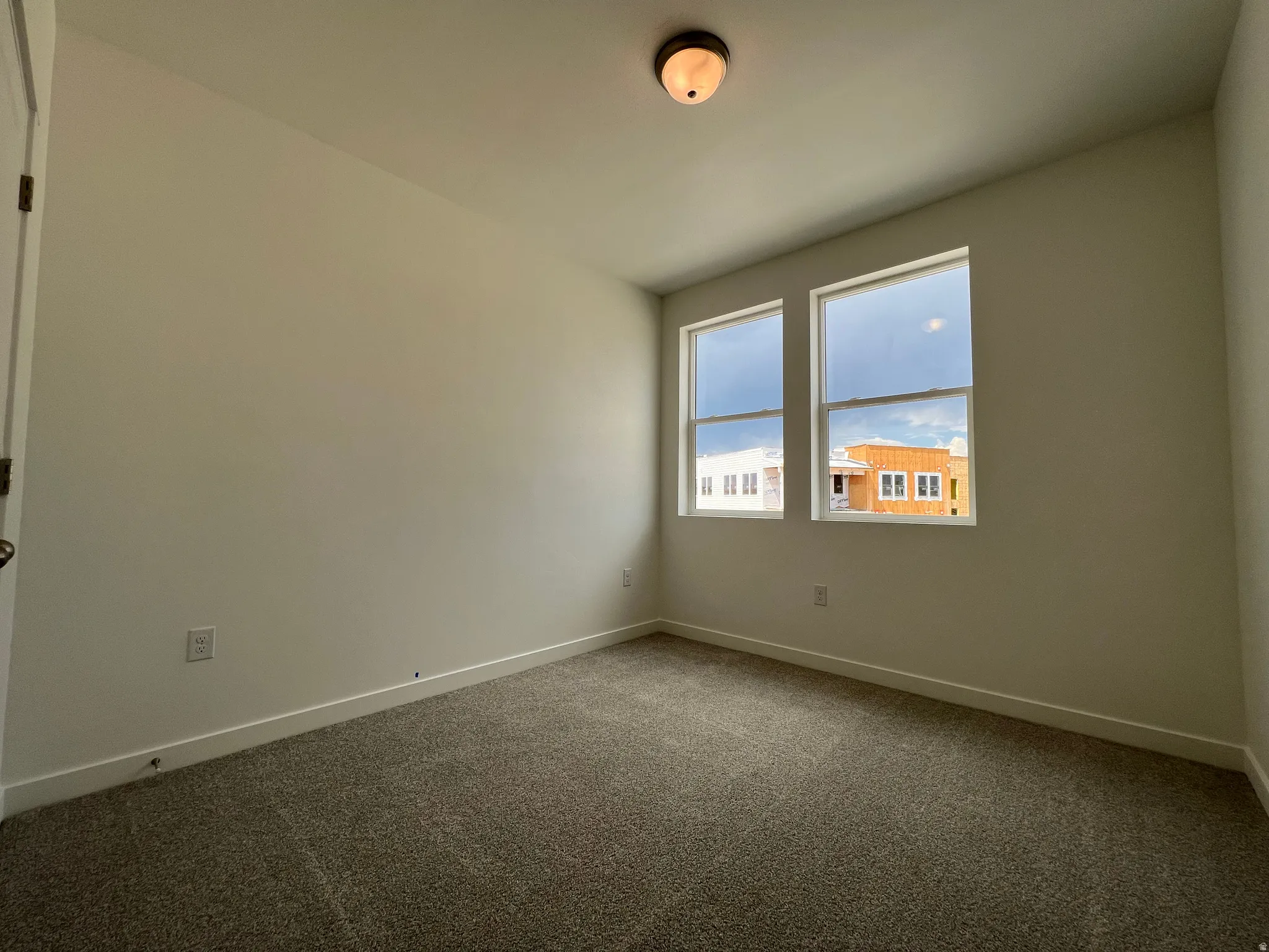 Neutral wall color, two windows, textured carpet, white baseboards, and a ceiling-mounted light fixture