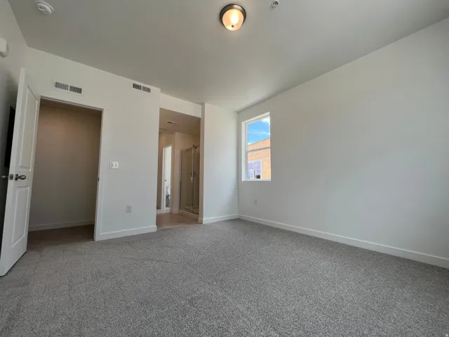 Carpeted room featuring a single window, overhead lighting, and an adjacent open doorway revealing a shower enclosure