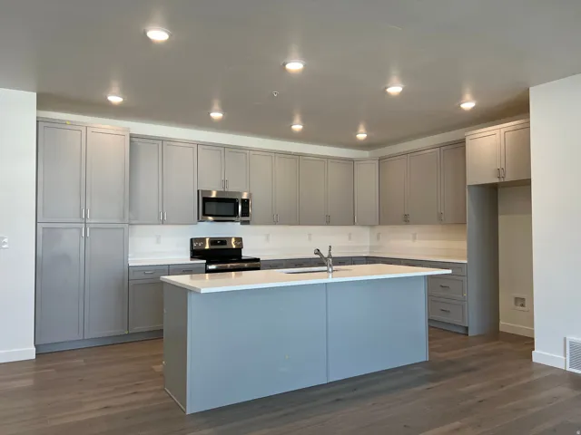 Modern kitchen featuring gray cabinetry, stainless steel appliances, a center island with sink, white countertops, and wood-finish flooring