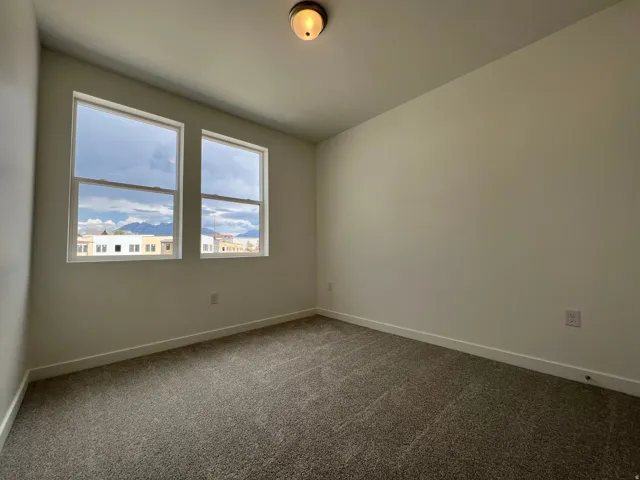 Bright interior space featuring two windows with surrounding white trim, neutral wall paint, and gray carpet flooring