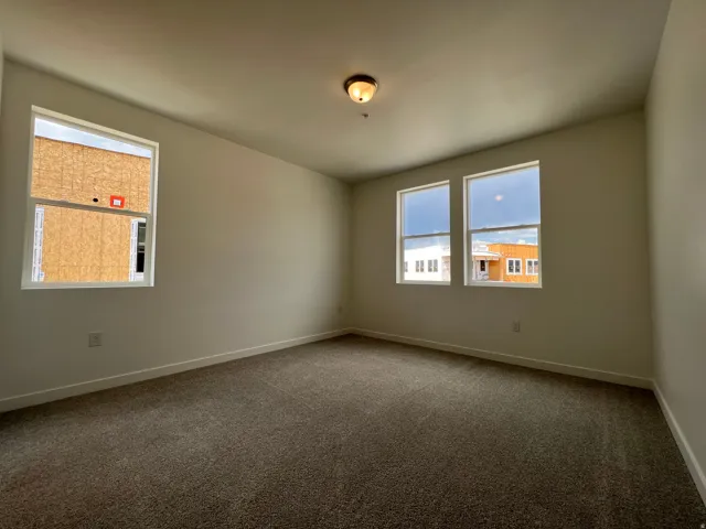 Spacious interior room featuring neutral-toned walls, textured carpet flooring, and a flush-mount ceiling light