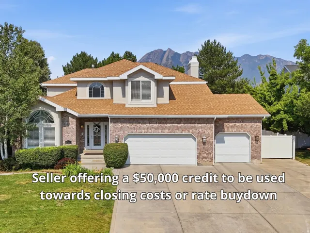 Brick and stucco exterior featuring a two-car garage, mature landscaping, a concrete driveway, and a shingle roof