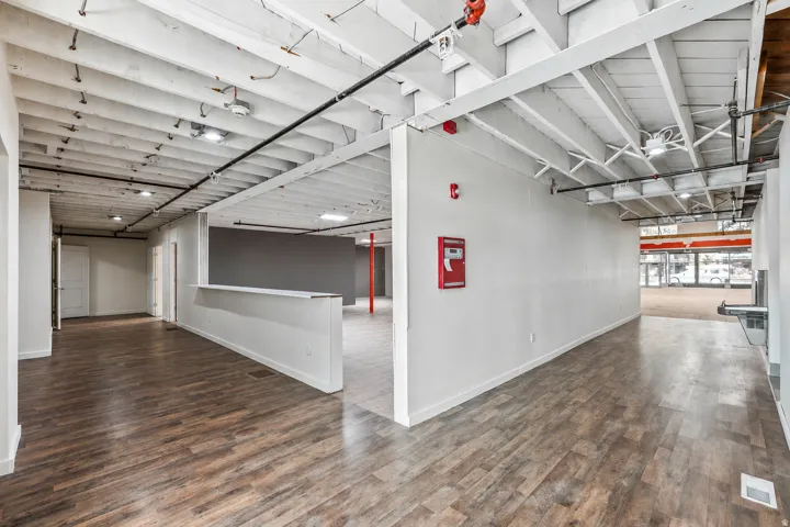 Open-concept commercial space featuring wood-finish flooring, exposed white ceiling joists, recessed lighting, and a partial partition wall