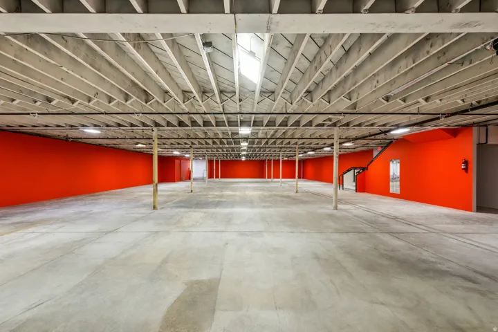 Expansive open space featuring concrete flooring, exposed ceiling beams, bright accent walls, and recessed lighting