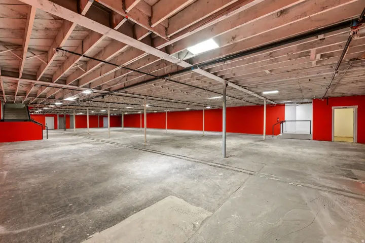 Spacious commercial basement featuring exposed ceiling joists, concrete flooring, and vibrant red accent walls