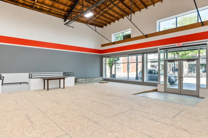 Spacious commercial interior featuring exposed wood ceiling trusses, expansive storefront windows, and a dedicated entry with glass doors